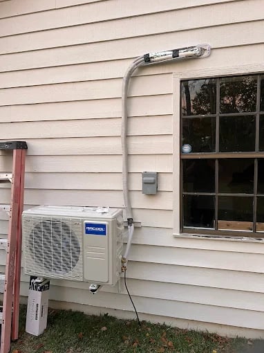 Mini-split air conditioner mounted on white siding near window