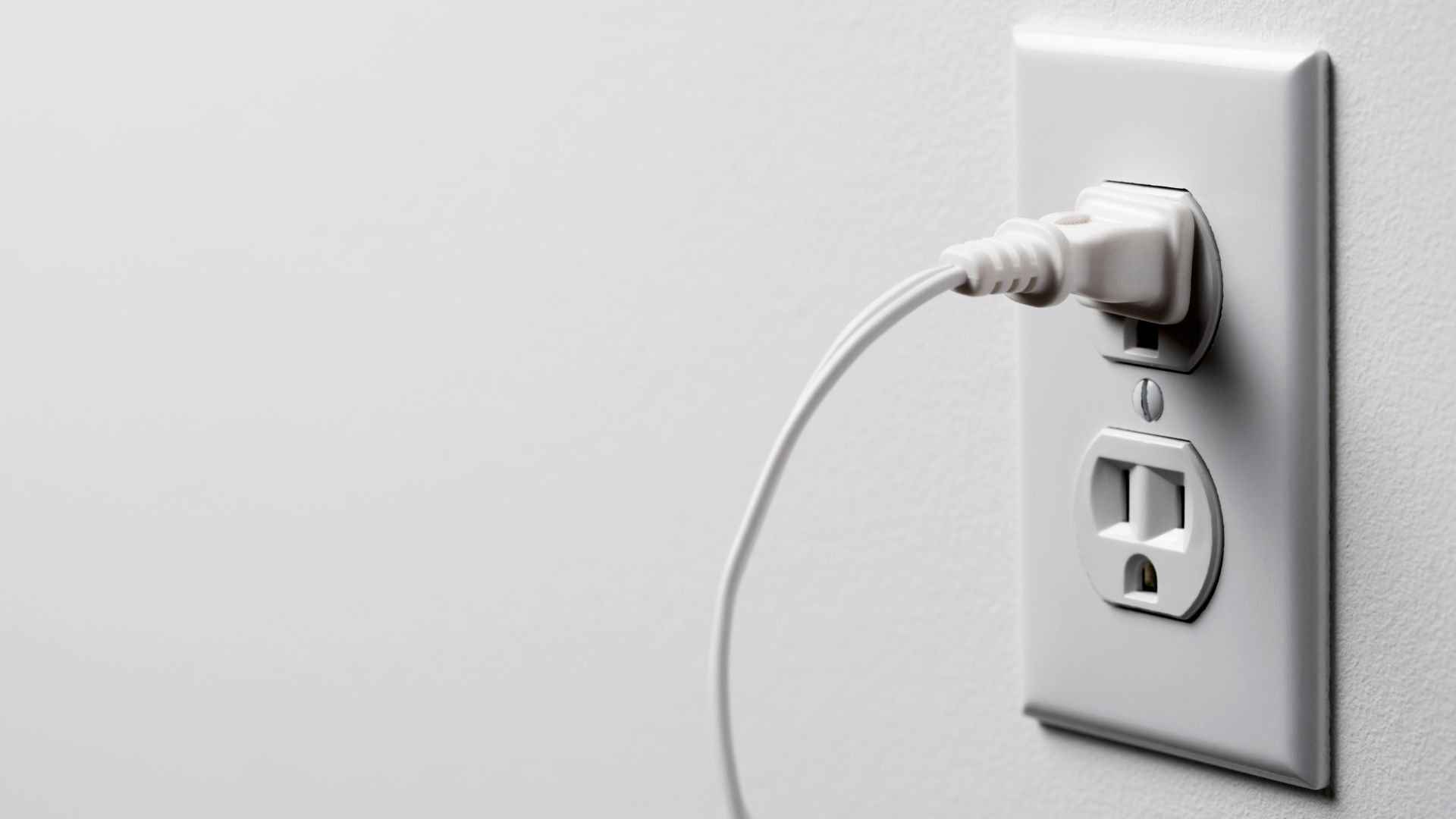 White electrical plug connected to outlet on minimalist light wall