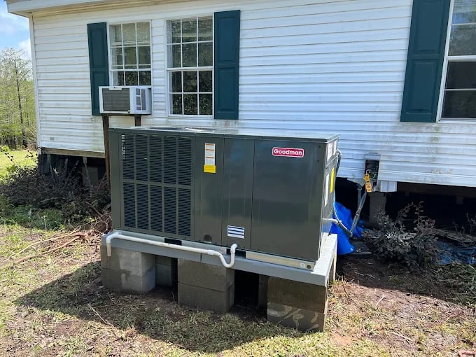 Goodman HVAC unit installed on concrete blocks next to white house