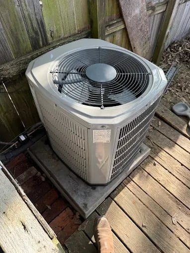 Air conditioning unit sitting on wooden platform near wooden fence