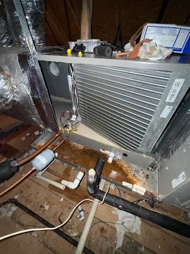 Old air conditioning unit with exposed pipes and wiring in cluttered space