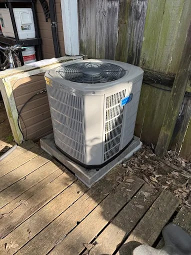 Air conditioning unit on wooden deck next to weathered fence