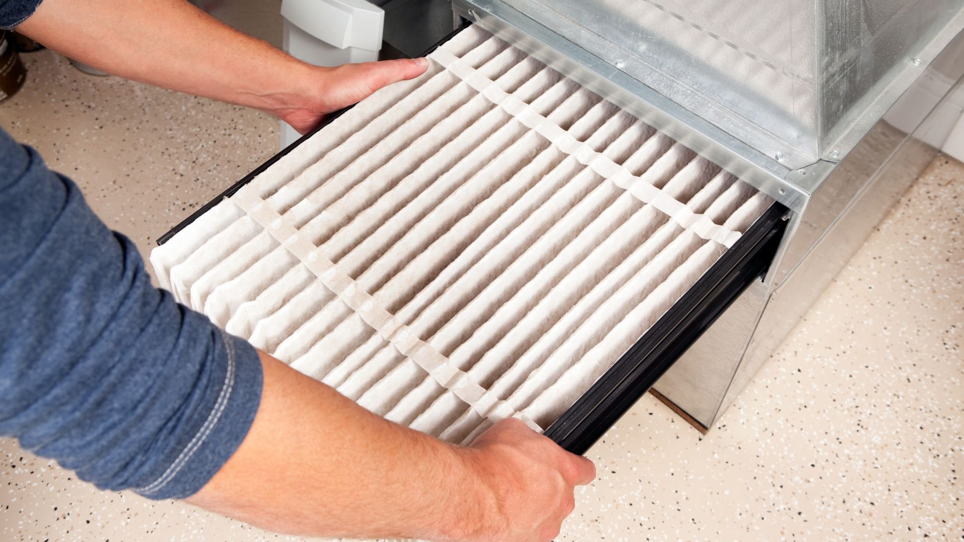 Hands replacing a clean white air filter in an HVAC system