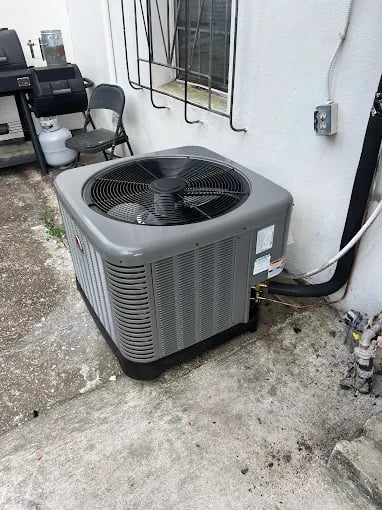 Gray air conditioning unit installed outside on concrete next to window