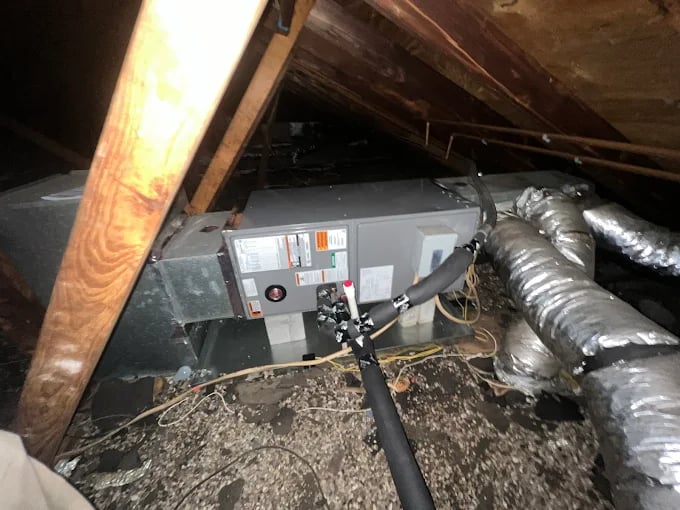 HVAC unit installed in dusty wooden-framed attic with insulated ductwork
