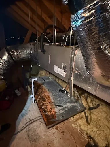 Rusty HVAC equipment and ductwork in a dimly lit attic space
