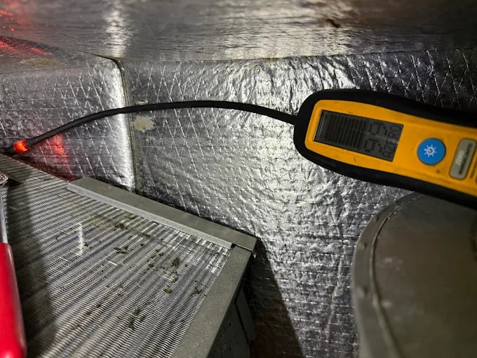 Yellow digital thermometer measuring temperature near metallic insulated surface