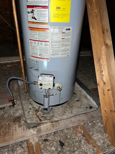 Gray water heater installed on wooden platform in dimly lit basement